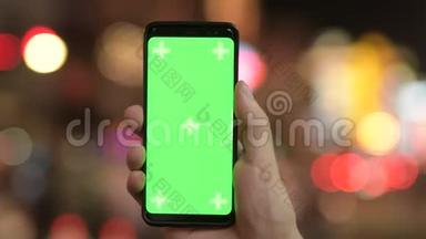 晚上用带绿色屏幕的屏幕的手机在灯光下进行特写